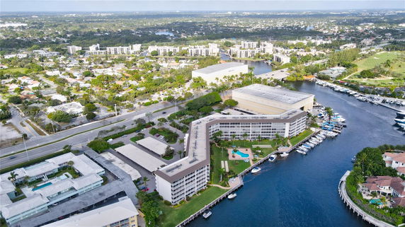 Aerial view of a waterfront building with a swimming pool, surrounded by residential and commercial areas.