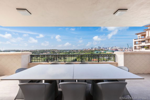 Balcony view from a high-rise building overlooking a city skyline and green areas.