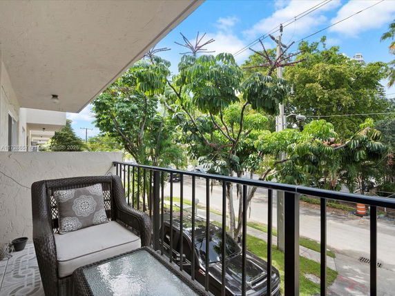 Balcony view overlooking trees and a street with parked cars.