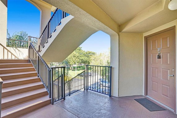 Balcony and stairs leading up to an apartment with visible surrounding trees and pathway.