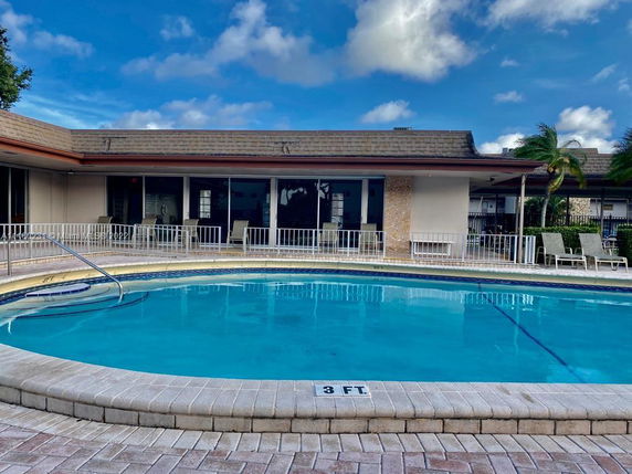 Outdoor swimming pool in front of a building with a seating area.
