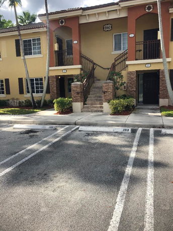 Parking area in front of a two-story residential building with stairs leading to an upper level.