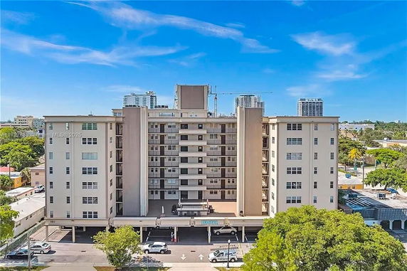 Front view of a multi-story residential building with parking spaces on the ground level.