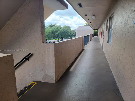 Corridor with view of trees and parked cars from a building.