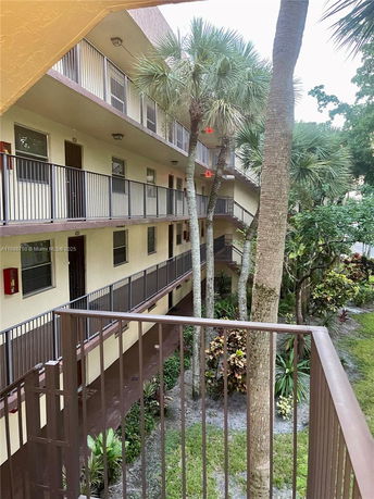 View of apartment building corridors from a balcony with trees and plants in the courtyard.