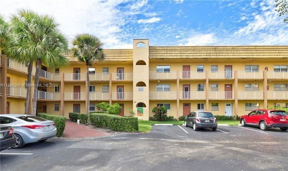 Front view of a three-story apartment building with balconies and parking spaces in front.