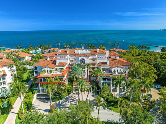 Aerial view of a coastal apartment complex with terracotta roofs and palm trees, overlooking the ocean.