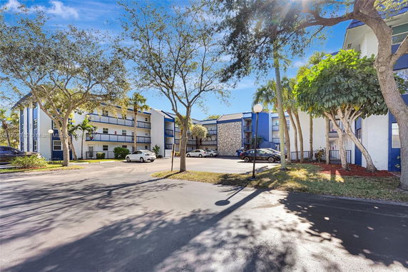 Front view of a multi-story residential building with a parking area and trees.