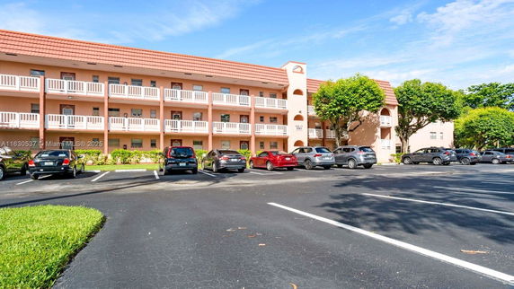 Front view of a three-story residential building with a parking area in front.