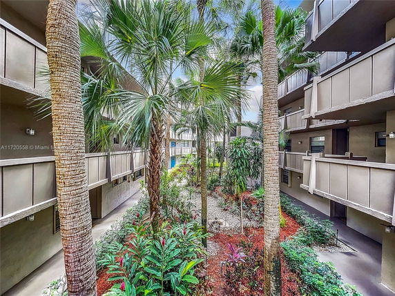View of an outdoor area within a multi-story residential building with balconies and palm trees.