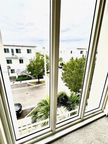 View from a window overlooking a street with modern houses and trees.