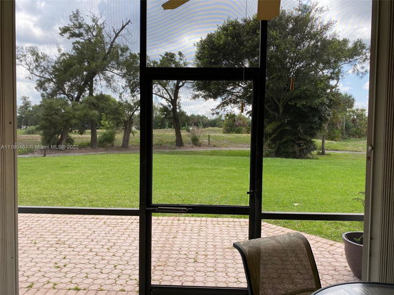 View from a patio with a glass door overlooking a grassy yard and trees.