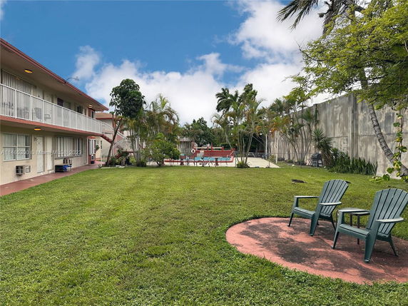 Backyard view of a building with an adjacent swimming pool and patio chairs.