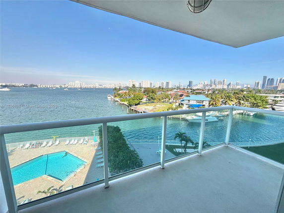 View from a balcony overlooking a body of water with city skyline and pool area.