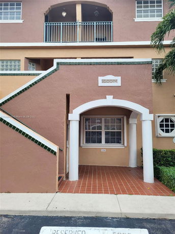Front view of a multi-story building with arched balcony and stairway entrance.