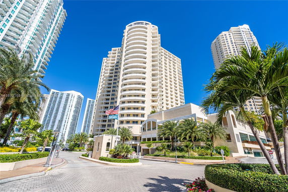 Front view of a modern high-rise building with balconies and a flag pole at the entrance.