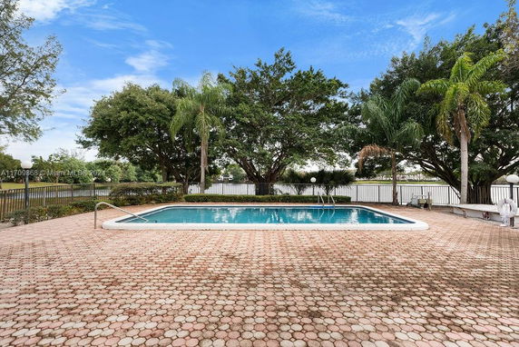 Outdoor swimming pool with surrounding paved area and trees.