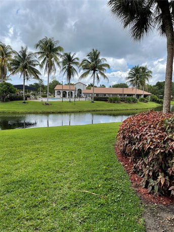 View of a house with palm trees and a pond in the foreground.