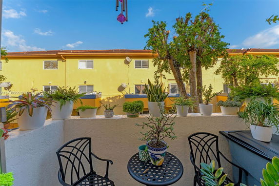 View from a balcony with potted plants overlooking a yellow building.