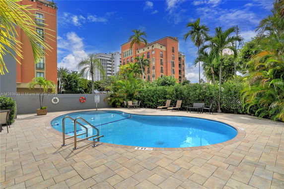 Outdoor swimming pool area with surrounding buildings and palm trees.