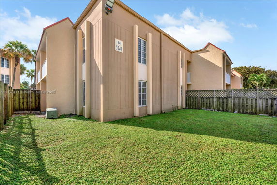 View of a two-story building with beige walls and a fenced grassy yard.