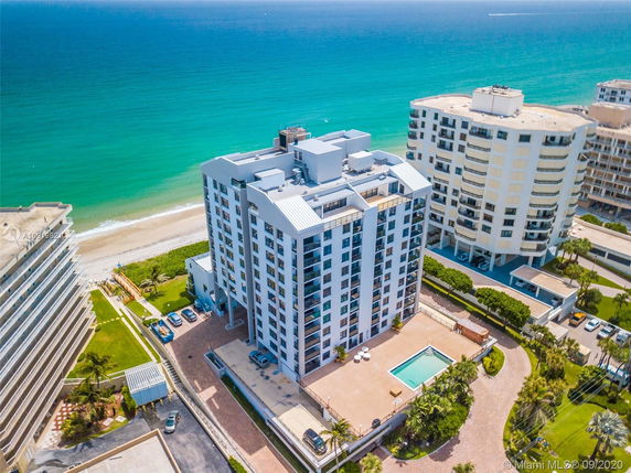 Aerial view of a multi-story beachfront building with a rectangular swimming pool and nearby high-rise structures.
