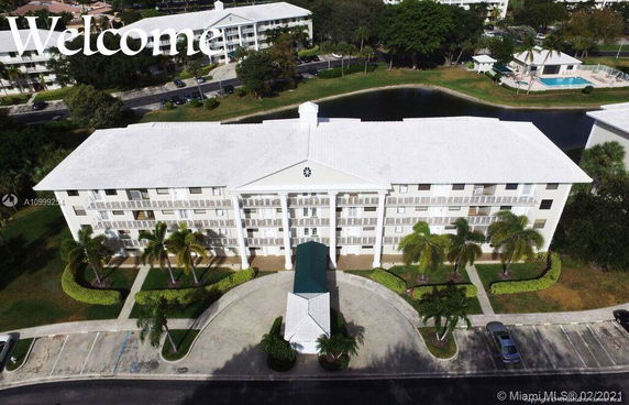 Front view of a multi-story residential building with a central entrance and surrounding parking area.
