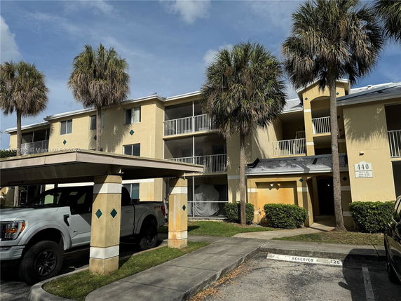 Front view of a three-story apartment building with balconies and palm trees.