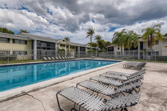 Outdoor swimming pool area with sun loungers and surrounding buildings.