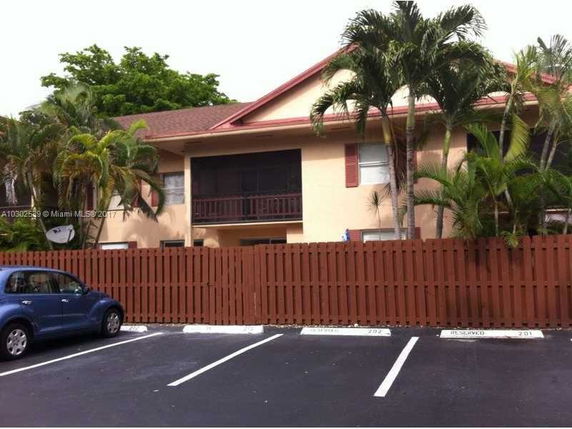Front view of a two-story house with wooden fencing and surrounded by palm trees.