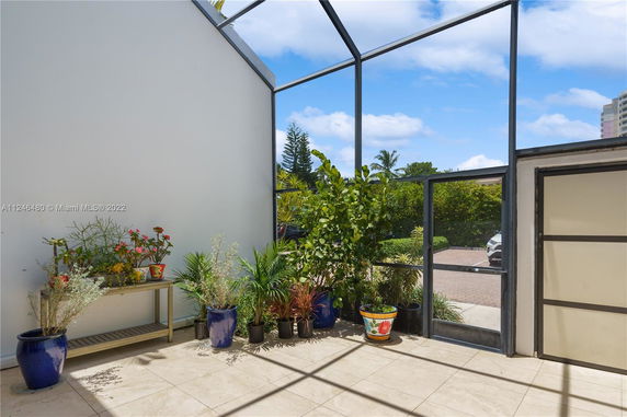 Patio area with potted plants and a view of parking space through glass walls.