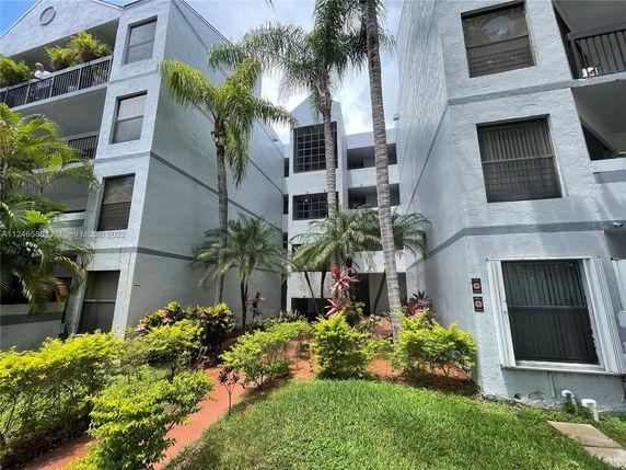 Front view of a multi-story residential building with balconies and surrounding greenery.