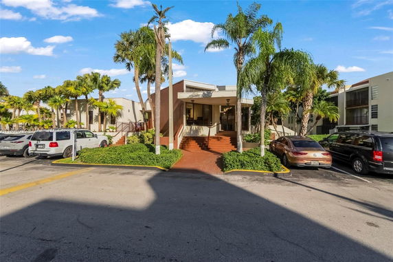 Front view of a building with stairs and a small entrance canopy, surrounded by palm trees.