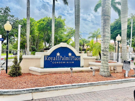 Entrance sign for Royal Palm Place Condominium surrounded by trees and lampposts.
