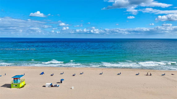 Panoramic view of a beach with a lifeguard tower, umbrellas, and ocean waves.