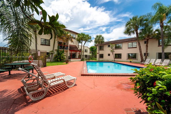 Outdoor swimming pool area with lounge chairs and adjacent multi-story buildings.