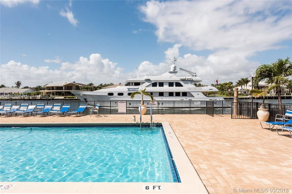 Outdoor swimming pool area with lounge chairs and a yacht in the background.