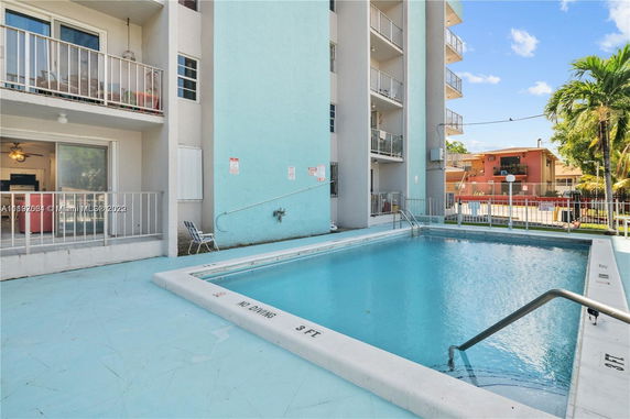 Outdoor swimming pool next to a multi-story building with balconies.