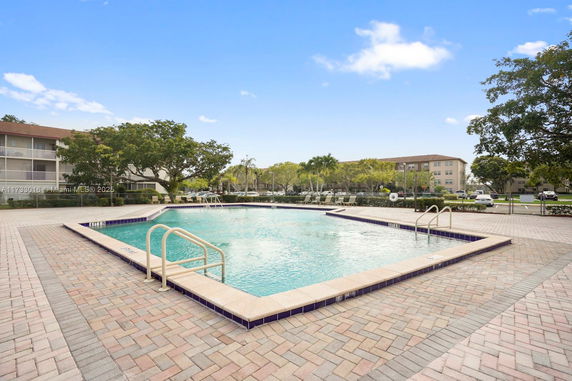 Outdoor swimming pool area with surrounding paving and trees in a residential community.