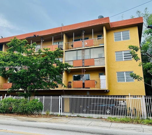 Front view of a multi-story apartment building with a yellow facade and balconies.