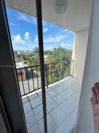 View from a balcony overlooking surrounding areas with vegetation and distant buildings.