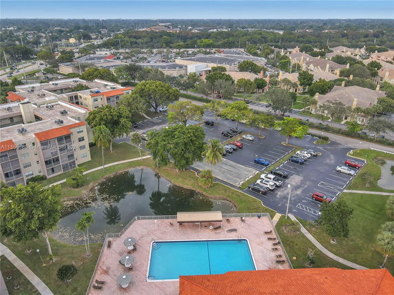 Aerial view of residential buildings, parking area, and swimming pool with suburban surroundings.