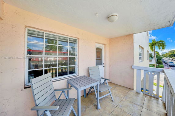 Outdoor balcony with table and chairs, view of nearby buildings and street.