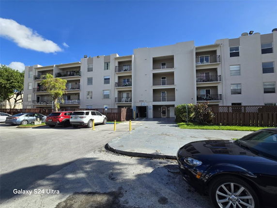 Front view of a multi-story apartment building with balconies and parking area.