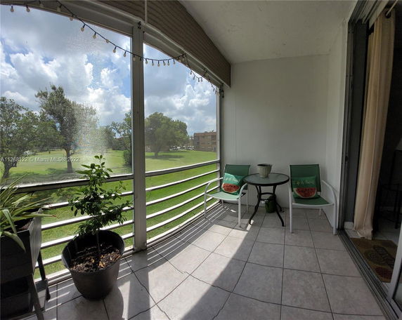 View from a balcony showing a grassy outdoor area with trees and distant buildings.