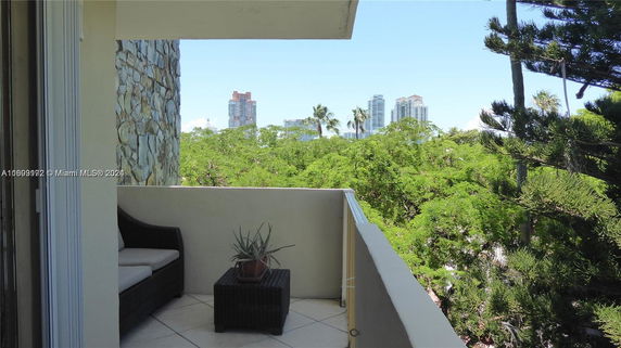 View from a balcony overlooking green trees and distant city buildings.