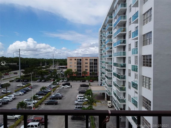 View of a multi-story apartment building with balconies and a parking lot below.