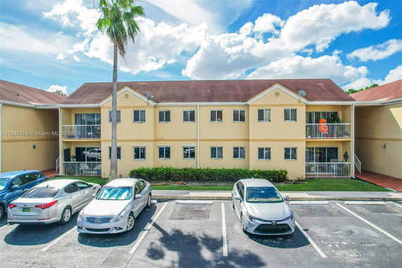 Apartment building with a front parking area and multiple cars parked.