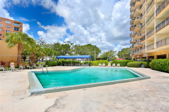 View of an outdoor swimming pool next to a multi-story building with balconies.