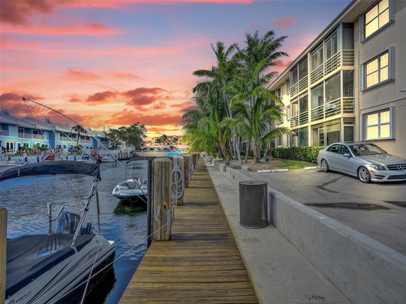 View of waterfront residential buildings with parked boats and a sunset in the background.